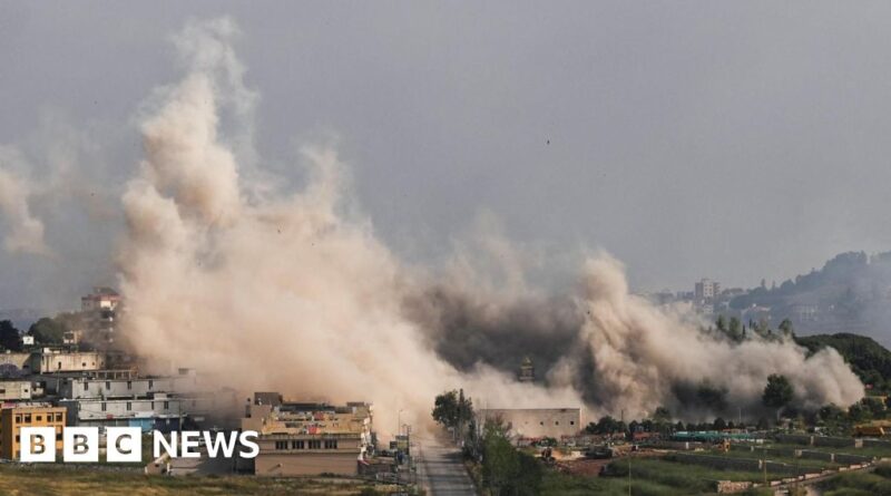 Dust plumes and smoke rise from a collapsing building in an urban area, with a BBC News logo in the lower left corner.