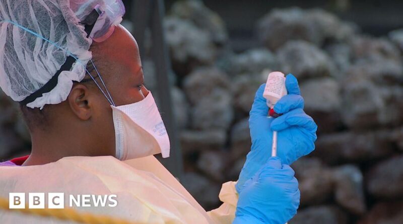 Healthcare worker in full PPE with mask and face shield drawing up a vaccine from a vial for administration. (BBC News)