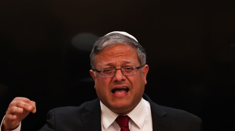 Man in a suit and kippah speaking passionately, one fist raised, intense expression against a dark background.