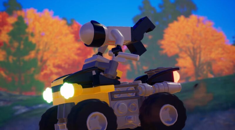 Lego-style motorbike with a white and gray robot figure perched on top, headlights on, autumn trees in the blurred background