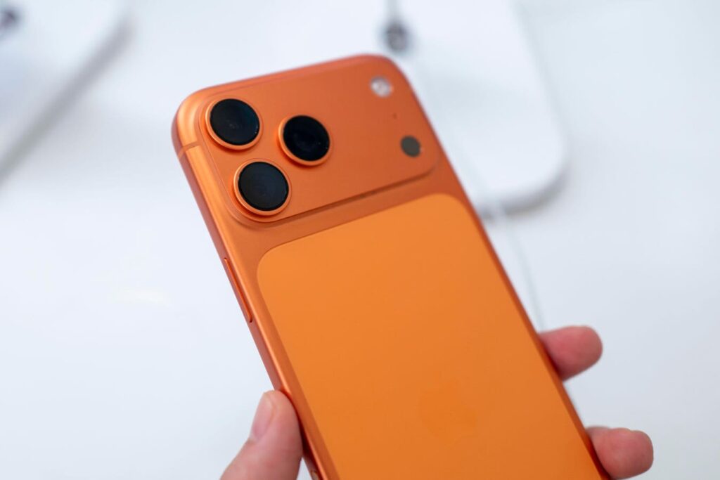 Orange smartphone held in hand, showing triple-camera rear setup on the back panel.