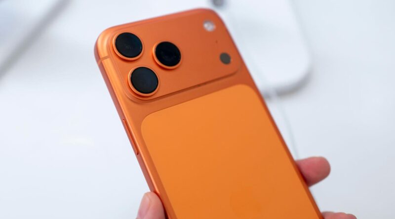 Orange smartphone held in hand, showing triple-camera rear setup on the back panel.
