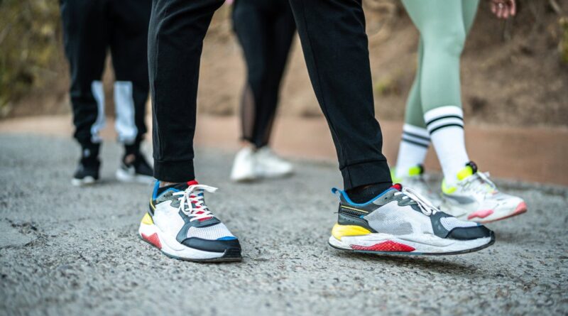 Close-up of multiple colorful sneakers on a gravel path as people stand or walk outdoors, suggesting a group activity or run.