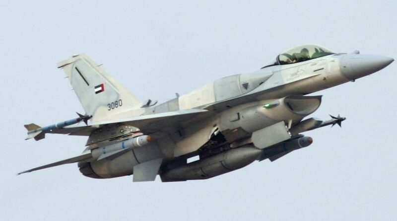 F-16 fighter jet in mid-flight with external fuel tanks and weapons, UAE insignia on the tail