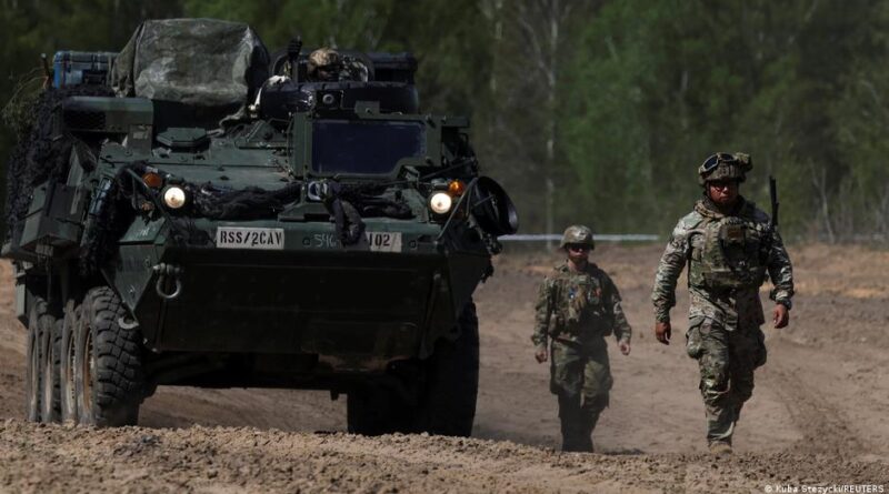 Armored personnel carrier on a dusty road, flanked by two soldiers in camouflage.