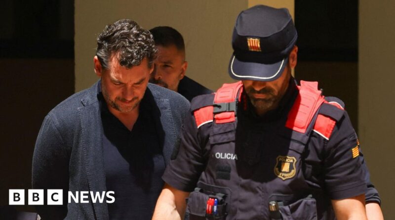 A man in a dark blazer walks beside a police officer in a navy uniform and red tactical vest, BBC News logo visible.