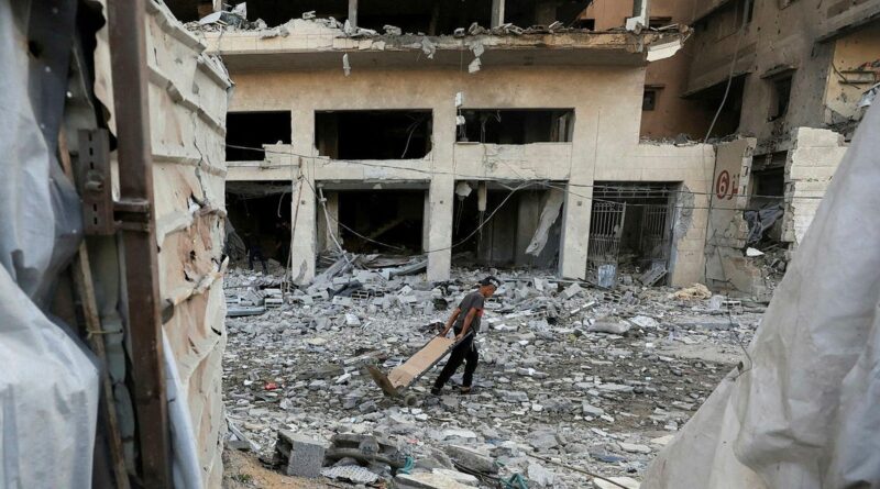 Man pushing a wooden cart through rubble in front of a ruined multi-story building.