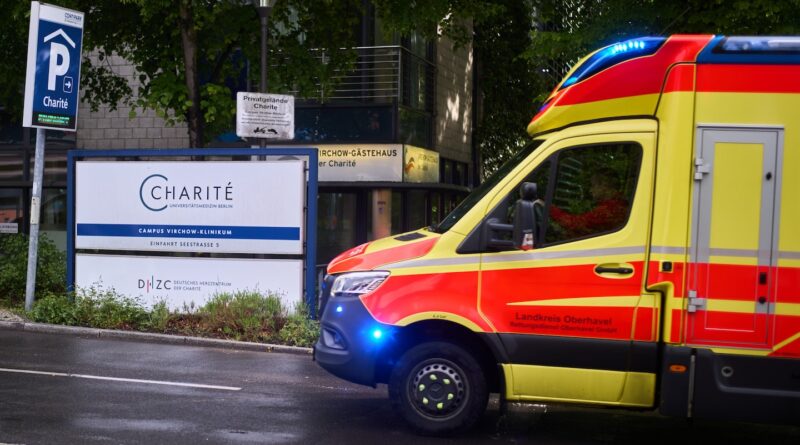 Yellow and red ambulance with blue lights parked on a street near a Charité campus sign in Berlin.