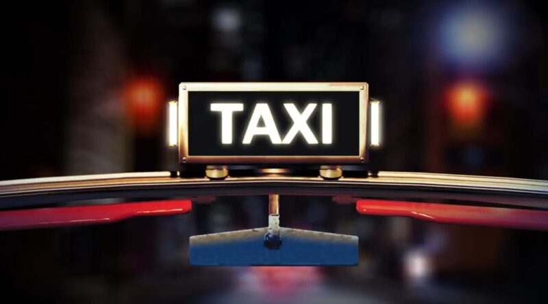 Illuminated TAXI sign on the roof of a car at night with blurred city lights in the background.