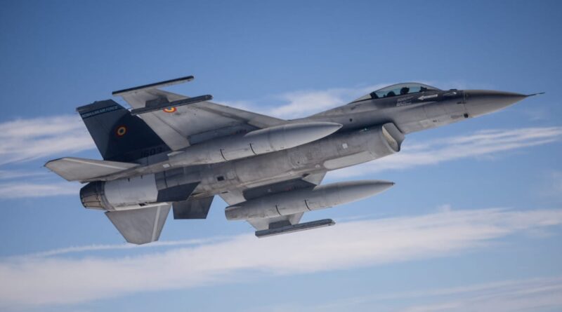 Romanian Air Force fighter jet in mid-flight against a blue sky, with external fuel tanks attached under the wings.