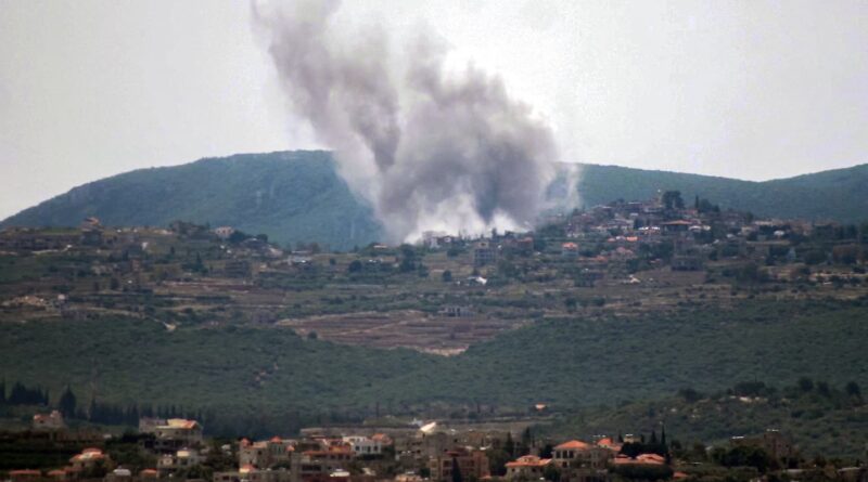 Smoke plume rising from a hillside village after an explosion nearby. A town sits on terraced hills with smoke obscuring part of it., A hillside town with a large column of smoke in the air from an incident nearby., Explosion in a hilly area; a tall smoke cloud rises above a cluster of buildings on the slope.