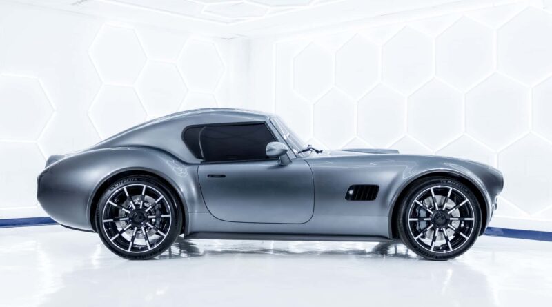 Side profile of a silver luxury sports car in a white showroom with hexagonal wall panels.