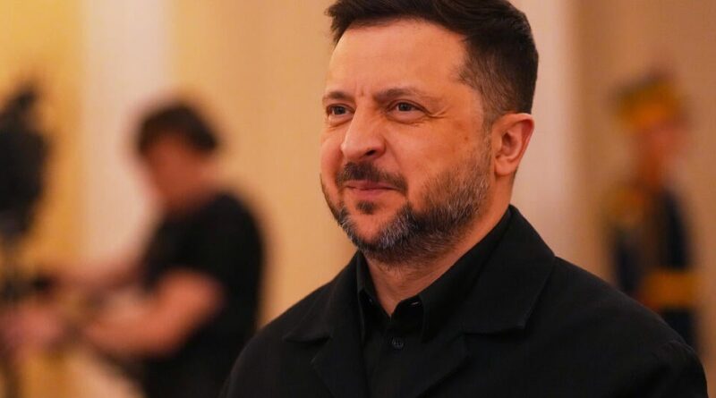 Man with short dark hair and beard in a black jacket at an indoor event, smiling slightly.