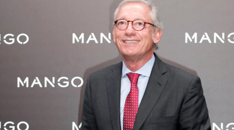 Smiling older man in a dark suit and red tie standing in front of a Mango backdrop.