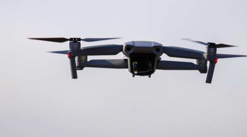 Gray quadcopter drone flying toward the viewer, propellers blurred, camera mounted at the front.
