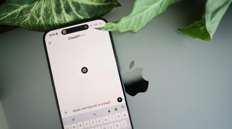 Close-up of an iPhone screen displaying ChatGPT, with green plant leaves above and a laptop Apple logo in the background.