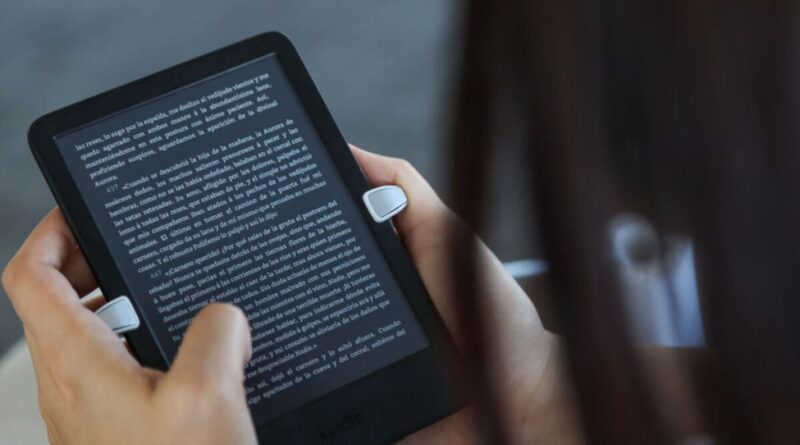 Person holds a black e-reader displaying small white text, fingers on the sides reading in Spanish.