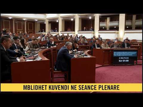 Parliamentary chamber with lawmakers seated around curved desks during a plenary session; bottom banner reads 'MBLIDHET KUVENDI NE SEANCE PLENARE'.
