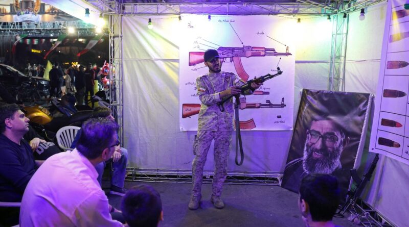 Soldier in camouflage demonstrates a rifle inside a weapon-drawing booth at an expo, with spectators watching.