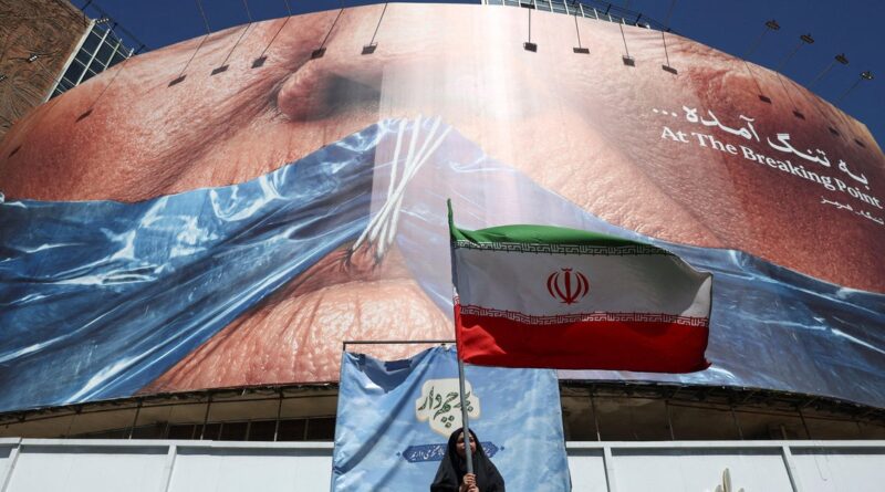 Massive curved billboard showing a close-up of skin with the words 'At The Breaking Point'; a person stands below, waving an Iranian flag in front of blue fabric.