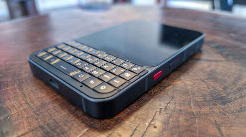 Old-style smartphone with a physical QWERTY keyboard resting on a wooden table.