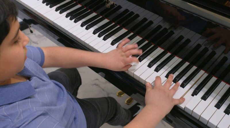 Child in a blue shirt plays a grand piano, hands on the white keys from a top-down angle.