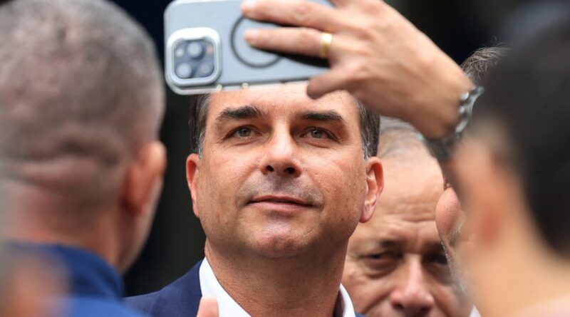Man in a suit taking a selfie with a smartphone held overhead, surrounded by people