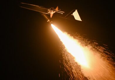 Night scene of a small aircraft releasing a bright rocket, with a long fiery exhaust plume trailing behind.