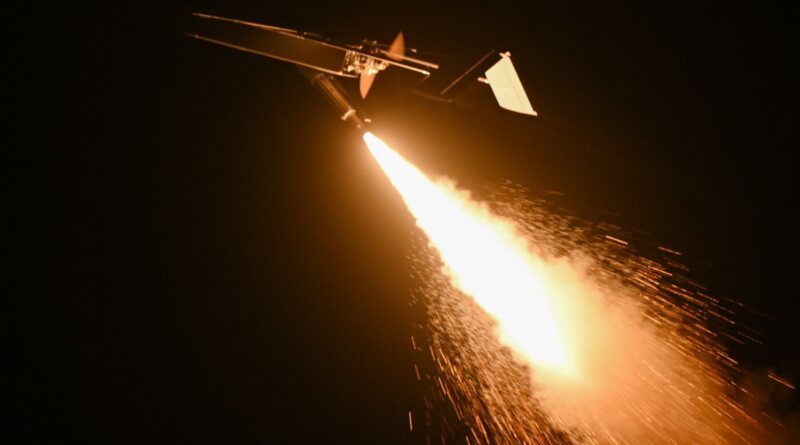 Night scene of a small aircraft releasing a bright rocket, with a long fiery exhaust plume trailing behind.