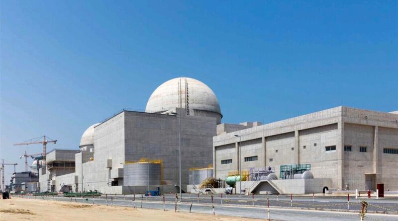 Industrial facility with large concrete buildings and dome-shaped structures under a clear blue sky; construction cranes visible in the background.