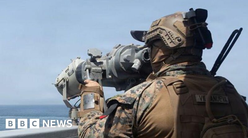Soldier in camouflage with helmet and tactical gear using a large optical scope on a naval ship, sea in the background.