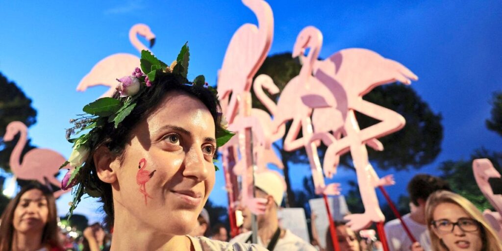 Woman wearing a flower crown at a festival, with large pink flamingo decorations in the background during blue hour.