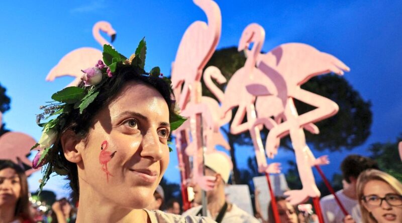 Woman wearing a flower crown at a festival, with large pink flamingo decorations in the background during blue hour.
