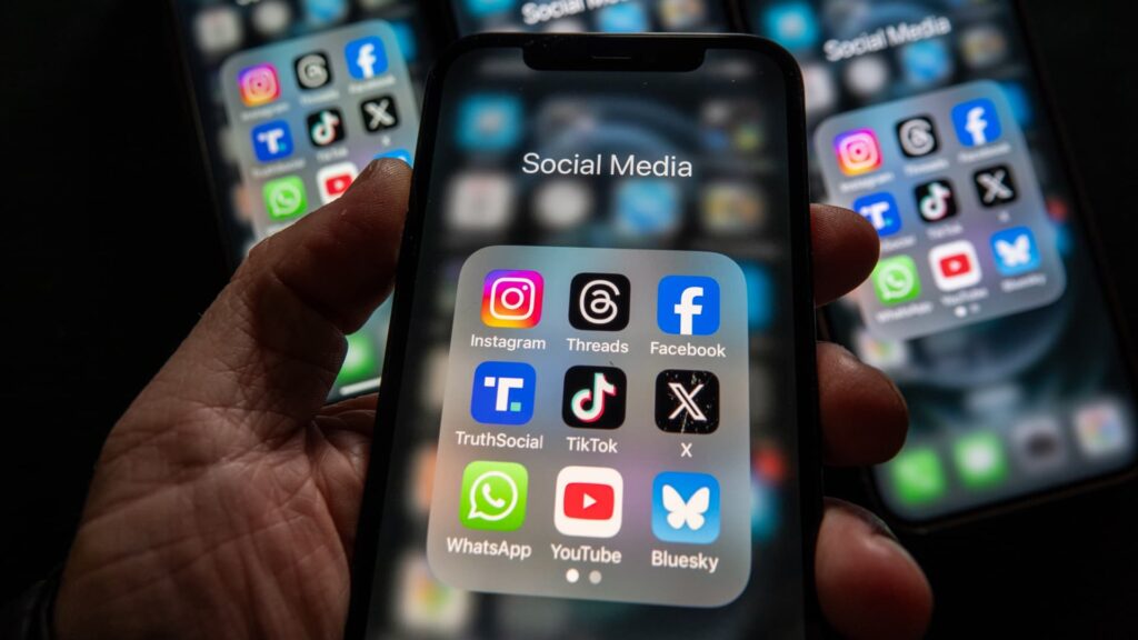 Smartphone screen showing a folder labeled Social Media with icons for Instagram, Threads, Facebook, TikTok, X, TruthSocial, YouTube, WhatsApp, Bluesky.