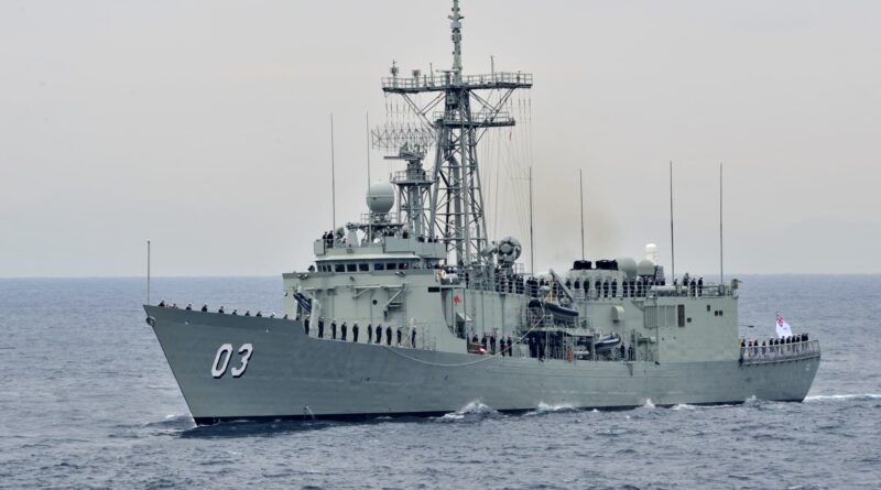 Gray military warship with sailors standing along the railing, sailing on calm sea with a large radar tower ahead.
