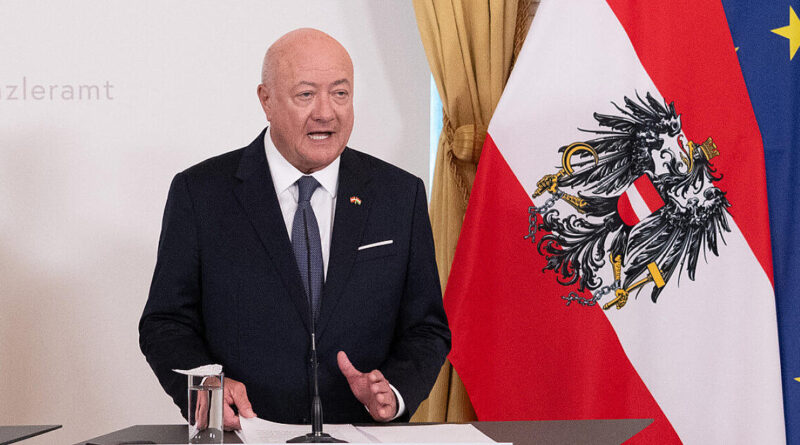 Bald man in a dark suit speaks at a podium with a microphone, with an Austrian flag and a European Union flag in the background.