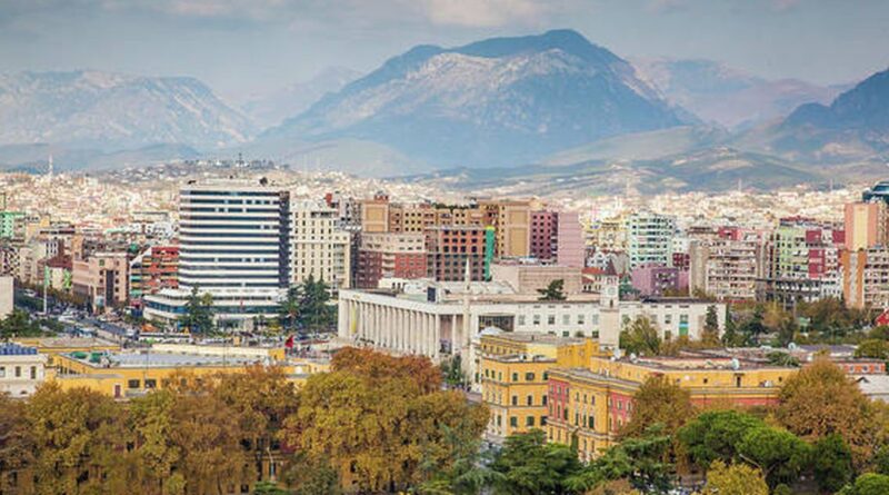City skyline with colorful buildings and a white curved office building, mountains in the distance, and autumn trees in the foreground.