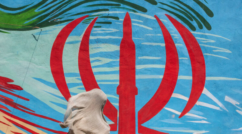 Person wearing a light cloth walks past a bright blue mural with a large red three-pronged symbol.