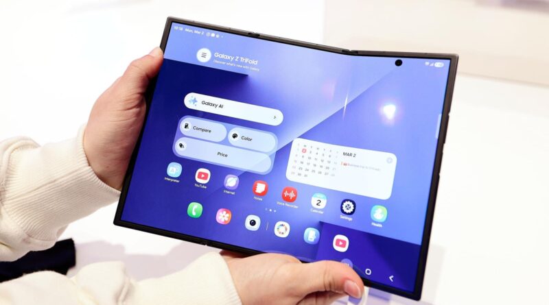 Person holding a blue Galaxy foldable tablet with app icons visible on screen in landscape mode