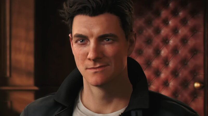 Portrait of a young man with dark hair and blue eyes, wearing a black leather jacket in a warmly lit room with a tufted red wall behind him
