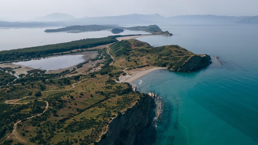Aerial view of a peninsula with green hills, rocky cliffs, and turquoise water along a sandy cove. (informative)