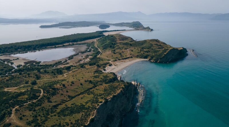 Aerial view of a peninsula with green hills, rocky cliffs, and turquoise water along a sandy cove. (informative)
