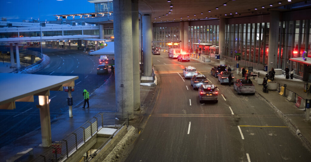 Airport terminal curbside with multiple cars and emergency flashing lights arriving or departing area near the entrance.