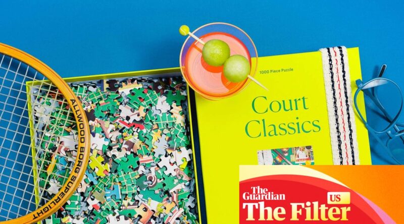 Bright flat lay with a yellow 'Court Classics' book, a colorful jigsaw puzzle, tennis racket frame, sunglasses, and a cocktail glass on a blue background.