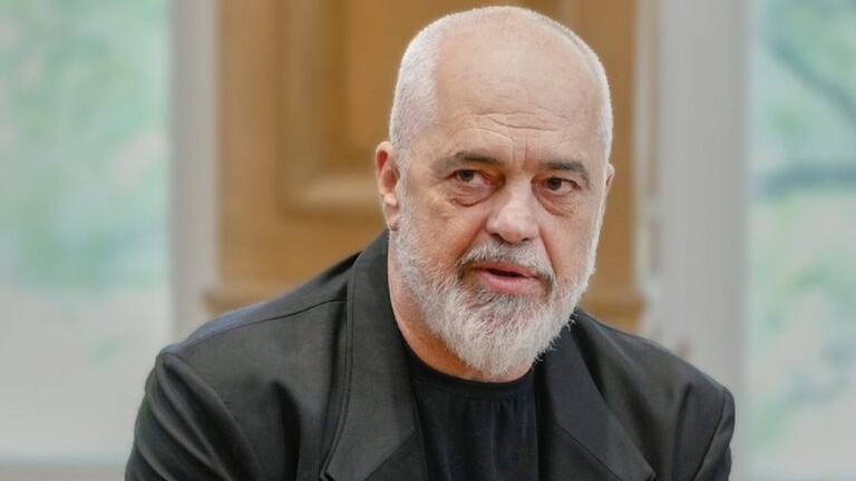 Bearded, bald man in a black jacket speaking in an indoor setting.
