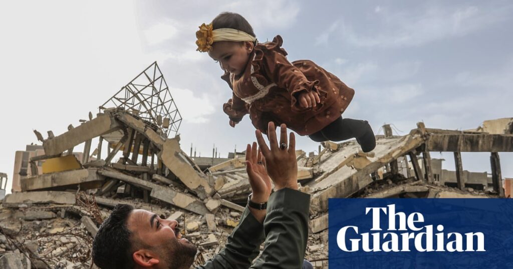 Man lifts a young girl over rubble in a war-torn scene, both smiling against a cloudy sky; Guardian watermark overlaps bottom right.