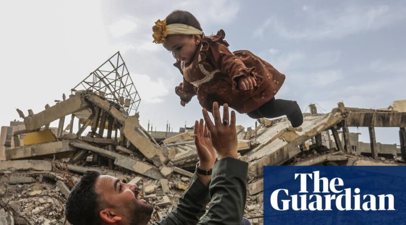 Man lifts a young girl over rubble in a war-torn scene, both smiling against a cloudy sky; Guardian watermark overlaps bottom right.