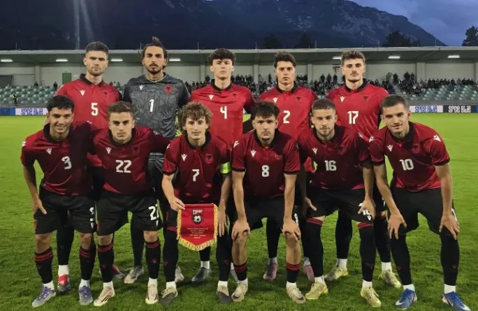 Men's soccer team in red jerseys posing for a group photo on a grass field, with a trophy banner held by the center player in front of the stands.