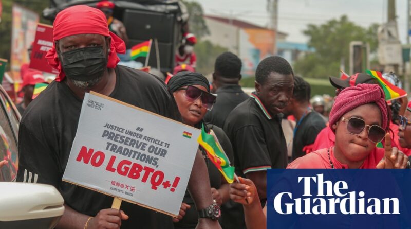 Protester in a red headscarf holding a sign that reads 'Preserve our traditions, No LGBTIQ+' during a street demonstration; crowd around with flags and a Guardian overlay logo in the corner.