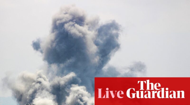 Massive plume of gray smoke rising into the sky from an explosion, with a red The Guardian logo banner overlaid in the bottom right.